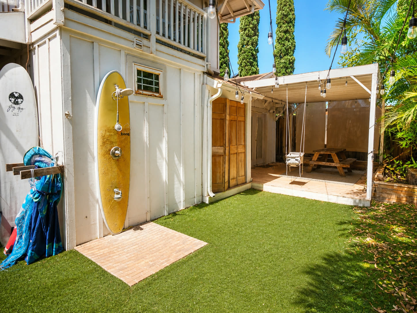 Backyard with outdoor surfboard shower, hammock, and string lights