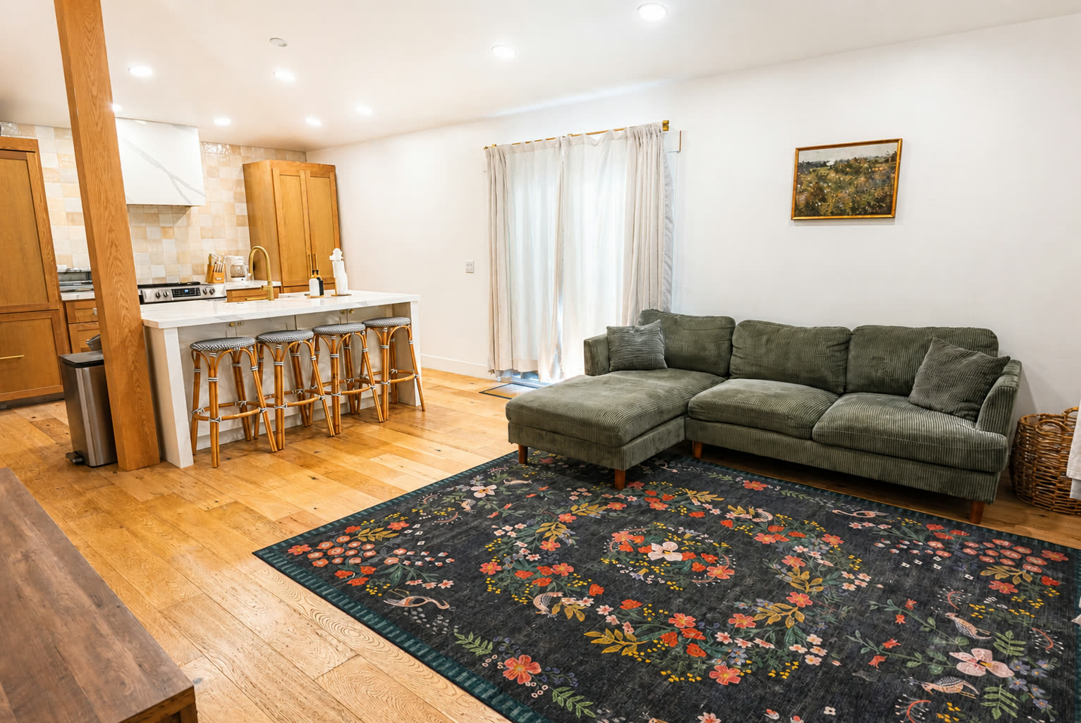 Open living area with green sectional and connected kitchen with bar stools